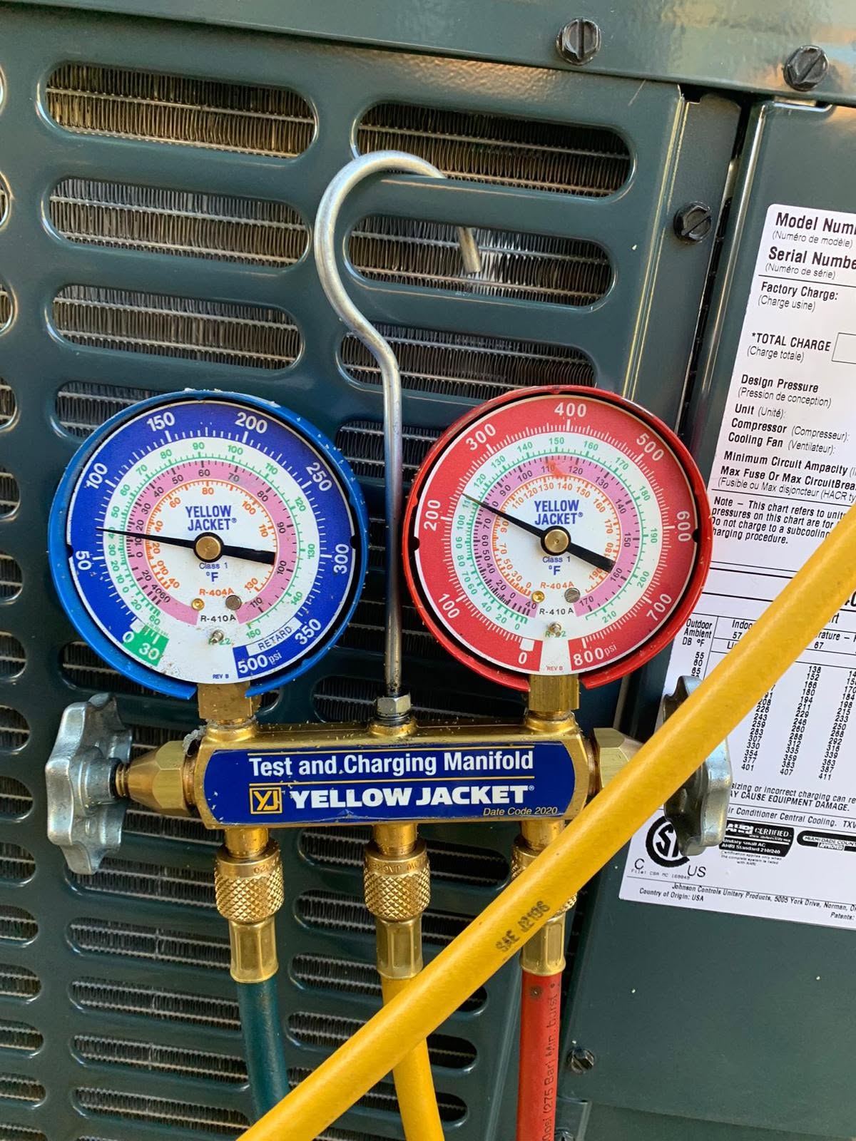 Close-up of a Yellow Jacket test and charging manifold with pressure gauges attached to HVAC equipment, displaying various pressure readings.